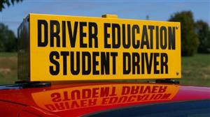 A yellow sign on top of a red car reads "Driver Education Student Driver" in large black letters.